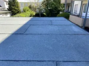 Flachdach mit sichtbaren Nähten zwischen Bäumen und Wohnhäusern