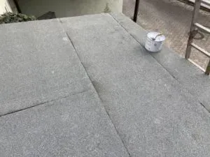 Graues Flachdach mit weißem Eimer am Rand, daneben Straße und Leiter