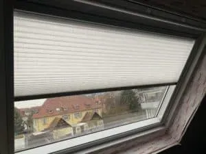 Teilweise geschlossene Jalousie an einem Dachfenster mit Blick auf Häuser