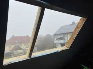 Fensterrahmen ohne Glas mit Blick auf Häuser und Bäume im Nebel