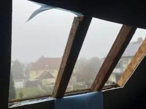 Loch im Dach mit fehlenden Platten, Blick auf ein nebliges Wohnviertel