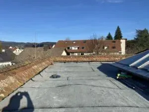Flachdach mit Dachrinne zwischen Häusern unter blauem Himmel