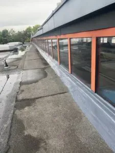 Lange Fensterreihe mit orangefarbenen Leisten auf einem Flachdach mit feuchten Stellen