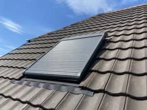 Kleines Dachfenster mit geschlossenem Metallrollladen in einem Ziegeldach