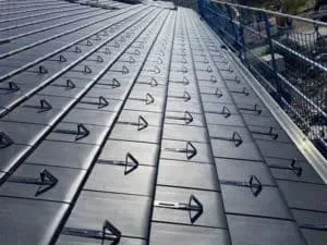 Nahaufnahme eines Metalldachs einer erfahrenen Dachdeckerei mit in regelmäßigen Abständen und ordentlichen Reihen installierten Schneefanggittern.