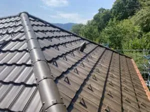 Braunes Ziegeldach mit Firstziegeln und kleiner Lüftung unter blauem Himmel