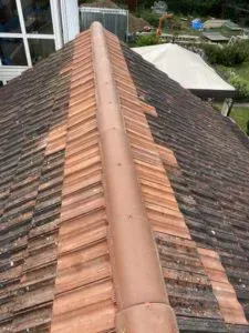 Hausdach mit First, auf dem alte und neu ausgetauschte Ziegel zu sehen sind