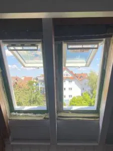 Zwei geöffnete Dachfenster mit Blick auf Bäume, Dächer und blauen Himmel