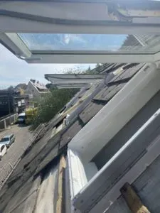 Offene Dachfenster auf einem schrägen Dach zeigen die Arbeit von Dachdeckermeistern und bieten an einem sonnigen Tag Blick auf eine Straße und Häuser.