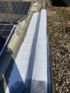 Neben Solarmodulen und Kies befindet sich eine weiß gestrichene Dachrinne, die von einer professionellen Dachdeckerei installiert wurde.