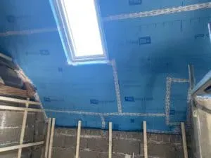 Mann mit Bart im schwarzen Poloshirt vor einer Backsteinmauer im Sonnenlicht