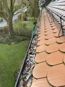 Blick von einem grauen Ziegeldach auf Häuser mit bunten Dächern unter bewölktem Himmel