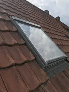 Geschlossenes Dachfenster in einem braunen Ziegeldach, darin spiegelt sich der Himmel