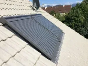 Zwei Solarmodule, die von einer professionellen Dachdeckerei auf einem schrägen Ziegeldach installiert wurden, mit Bäumen und Häusern im Hintergrund.