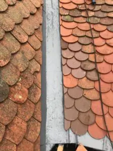 Alte, verwitterte Dachziegel links und neue Ziegel rechts, getrennt durch den First
