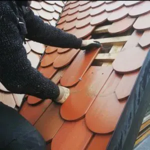 Dachdecker mit Handschuhen verlegt rote Dachschindeln auf einem Schrägdach
