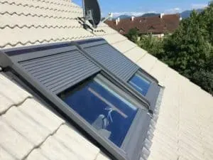 Zwei Dachfenster mit geschlossenen Fensterläden auf einem schrägen Ziegeldach, fachmännisch von einer Dachdeckerei gefertigt, unter klarem Himmel.