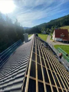 Dach im Bau mit Holzbalken und Metallziegeln, Blick auf eine ländliche Landschaft