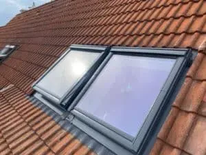 Zwei Dachfenster in einem Schrägdach mit roten Ziegeln unter blauem Himmel