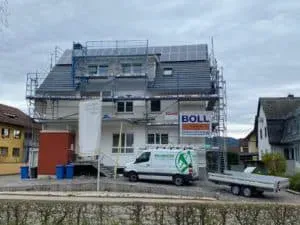 Eingerüstetes Haus mit Solarzellen auf dem Dach, davor ein weißer Transporter