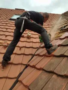 Ein Dachdeckerei-Fachmann schneidet Dachziegel mit einer Motorsäge und steht dabei sicher auf einem geneigten Ziegeldach.