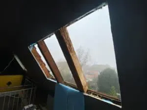 Kaputtes Dachfenster ohne Scheibe, freiliegende Holzbalken, draußen Nebel