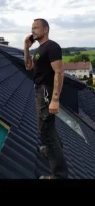 Mann steht auf einem Schrägdach und telefoniert, dahinter die Landschaft