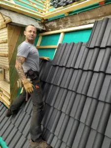 Dachdecker verlegt schwarze Dachziegel auf einem Schrägdach im Bau