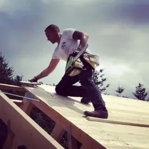 Dachdecker verlegt Holzplatten auf einem Schrägdach, dahinter Bäume