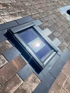 Neu eingebautes Dachfenster mit schwarzer Einfassung in einem Ziegeldach