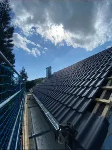 Dunkles Ziegeldach mit Gerüst unter leicht bewölktem Himmel