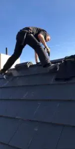 Person in schwarzer Kleidung klettert auf ein Schrägdach, blauer Himmel