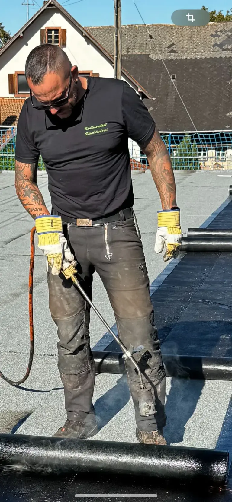 Ein Mann erhitzt an einem sonnigen Tag Dachmaterial mit einer Fackel.