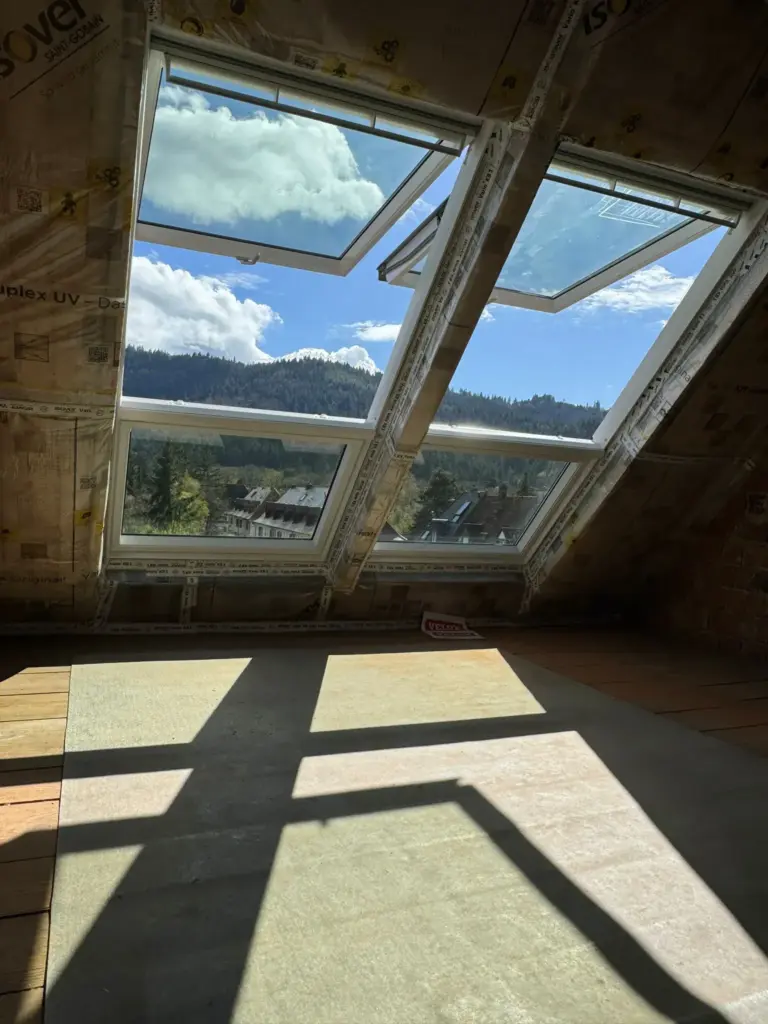 Große schräge Fenster im Dachgeschoss lassen Sonnenlicht herein und bieten einen malerischen Blick auf die Berge und Wälder draußen.